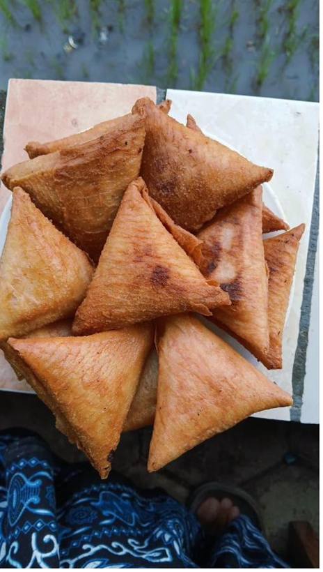 Lumpia segitiga baru diangkat dari wajan, difoto di pinggir sawah.